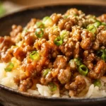Honey garlic ground turkey over jasmine rice in dark bowl topped with green onions and sesame seeds easy high protein dinner recipe