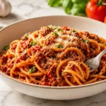 Italian ground beef pasta with rich tomato meat sauce, parmesan, basil, and fork in a white bowl on marble countertop
