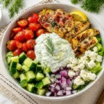 Greek chicken bowl with grilled chicken, tzatziki, cucumber, cherry tomatoes, feta cheese and red onion on marble background