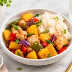 Pineapple chicken rice bowl with bell peppers, sesame seeds, and fluffy rice served in a ceramic bowl for dinner.