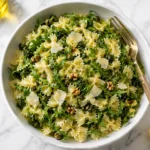 Lemon arugula pasta salad with bowtie pasta, parmesan, walnuts, capers, and fresh lemon in a white serving bowl.