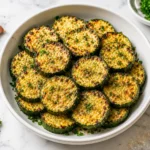 Garlic Parmesan roasted zucchini in a white ceramic bowl on a marble countertop, topped with fresh parsley and crispy cheese.